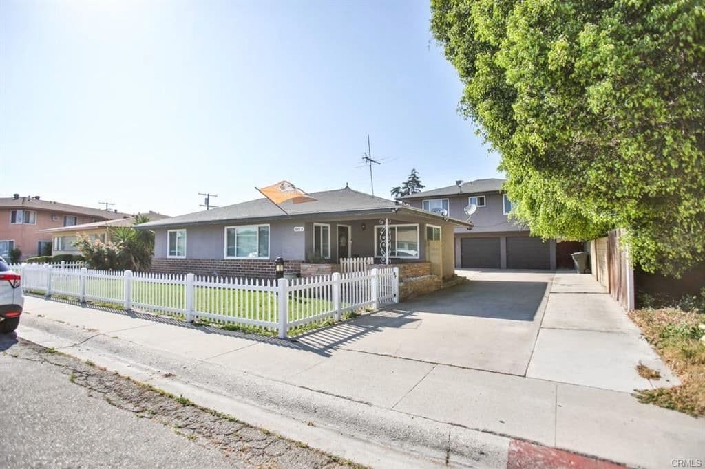 Street frontage of 525 W Hampshire Ave: a single-storey triplex behind a white picket fence, with a lawn, driveway and two garage doors to the right.